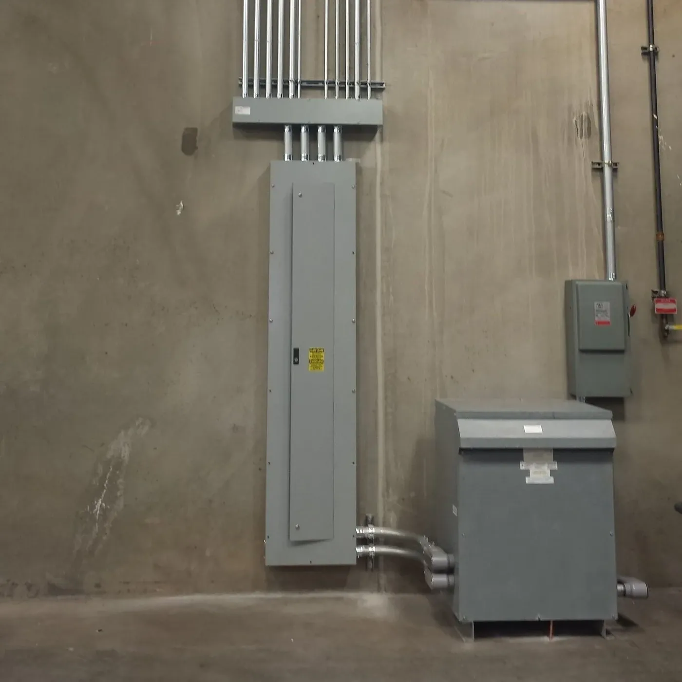 New industrial distribution panel and step-down transformer on a concrete wall, conduit running up to the ceiling