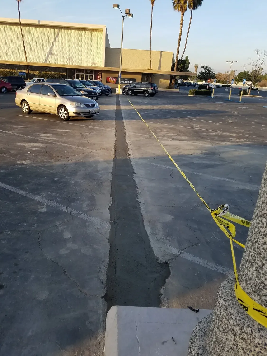 Fresh trench cut through a parking lot for an underground electrical run, taped off